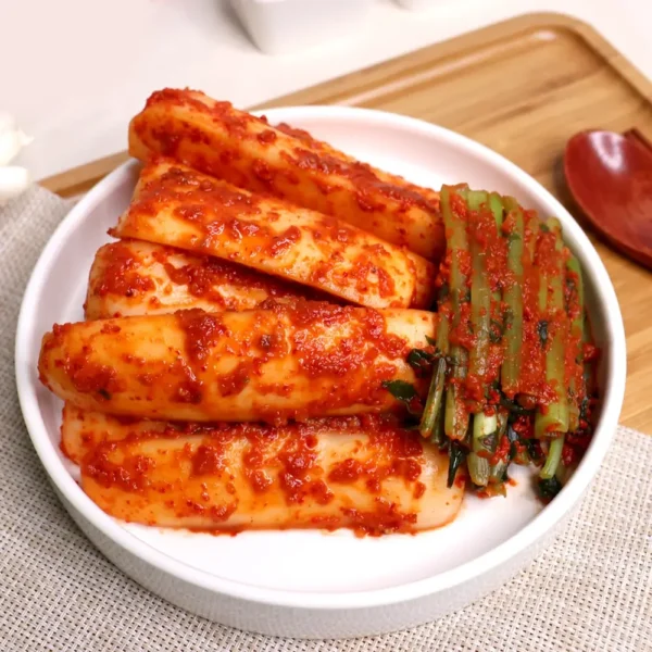 Bowl of HanMaru altari-kimchi (young radish kimchi) coated in vibrant red sauce, with tender stems on the side.
